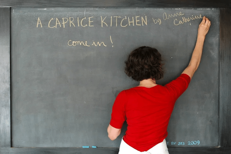 Anne Catherine Kruger writing “A Caprice Kitchen by Anne Catherine — come in!” on a chalkboard at her Ballard restaurant.
